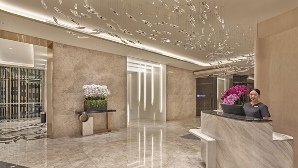 A modern hotel lobby with a marble reception desk, a potted plant, and a decorative ceiling light fixture. - Orchid Hotel (Singapore)