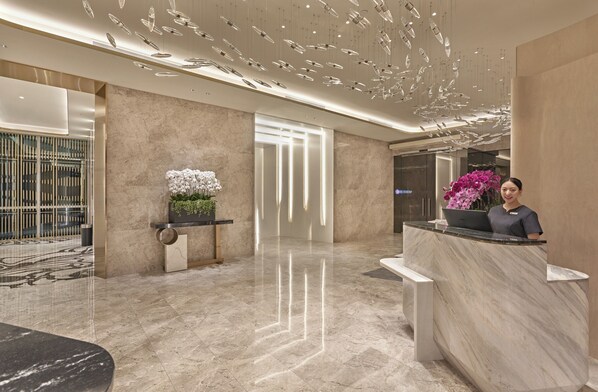 A modern hotel lobby with a marble reception desk, a potted plant, and a decorative ceiling light fixture. - Orchid Hotel (Singapore)