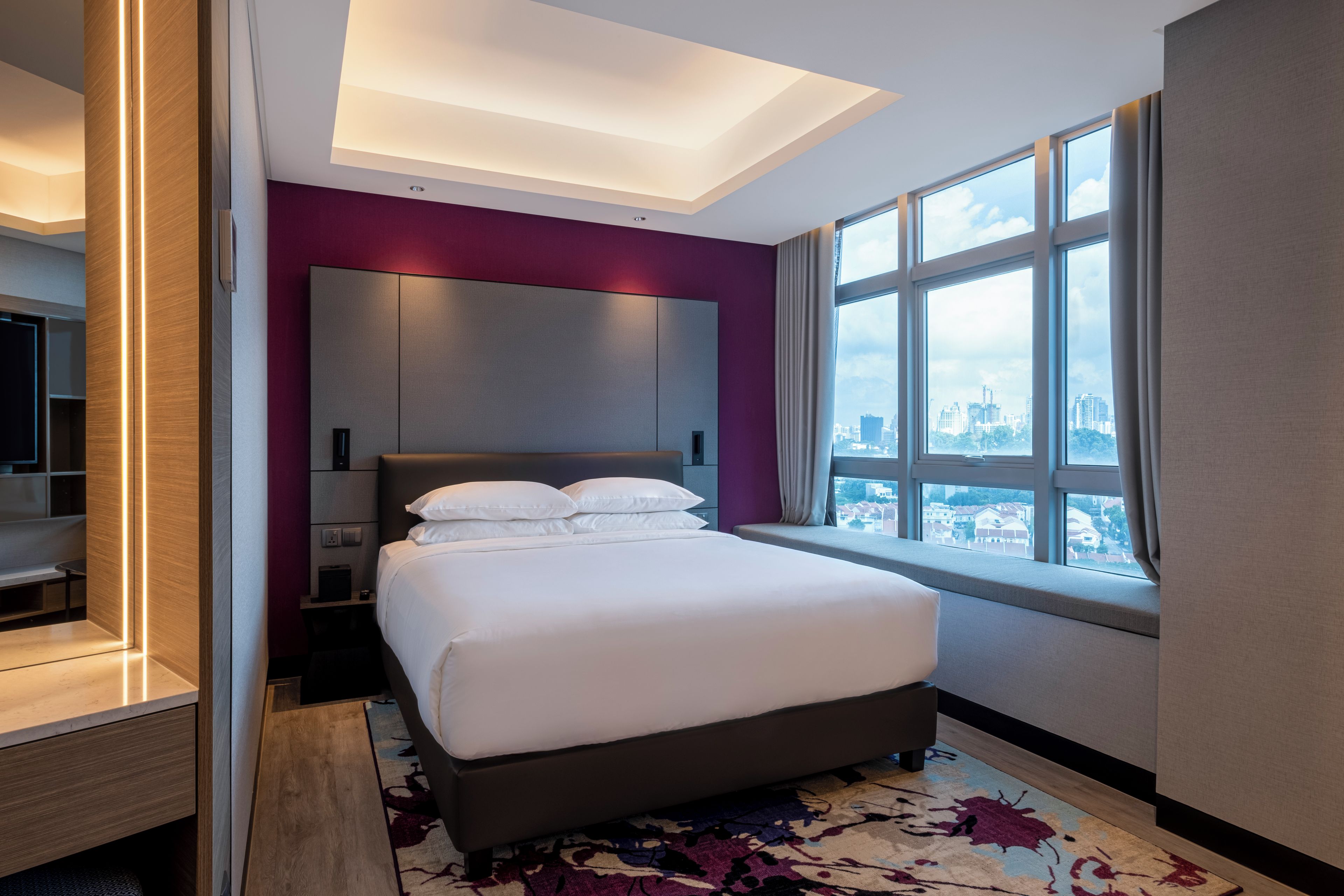 A modern hotel room with a large bed, a city view, and a walk-in closet.
