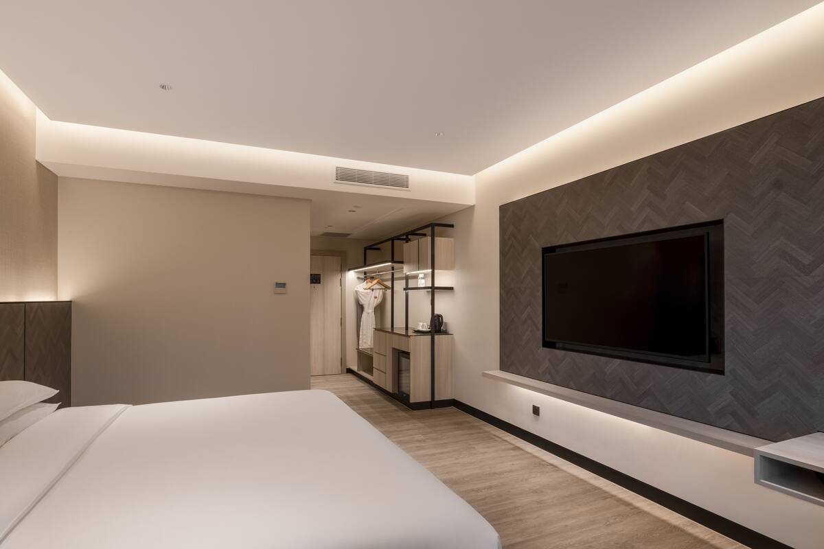 Quarto de hotel moderno com uma cama grande, uma TV fixada na parede e um closet espaçoso com espelho e prateleiras.