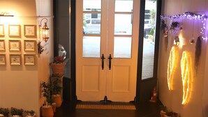 A hotel entrance with a double door, potted plants, framed certificates on the wall, and decorative lights. - Le Mong Hotel (Seoul)