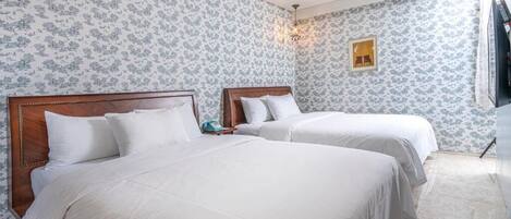A hotel room with two beds, floral wallpaper, a chandelier, and a framed picture on the wall.