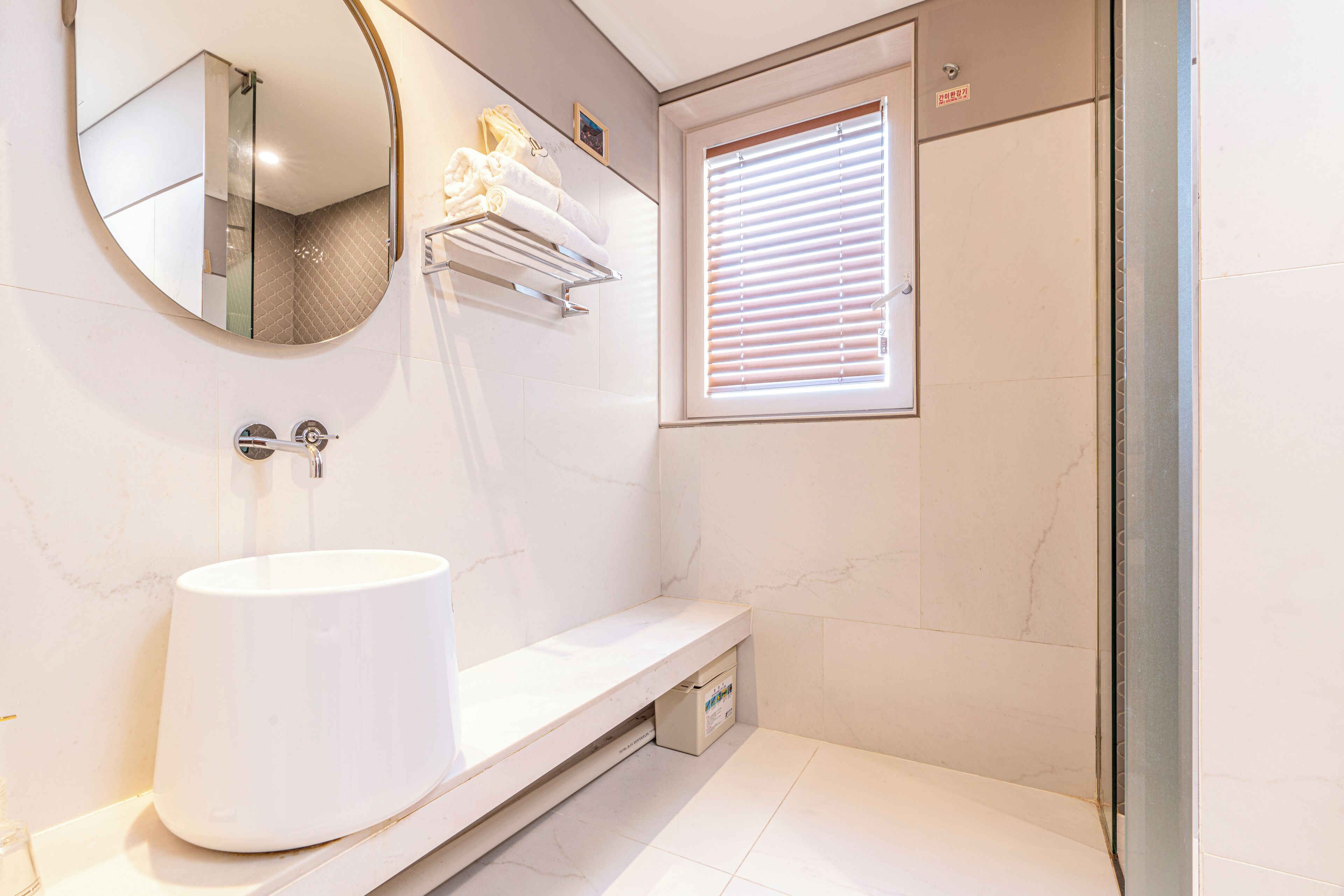 A bathroom with a white sink, a mirror, a towel rack, and a window with blinds.