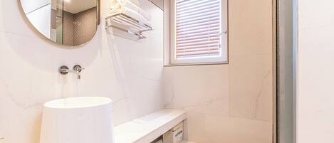 A bathroom with a white sink, a mirror, a towel rack, and a window with blinds.