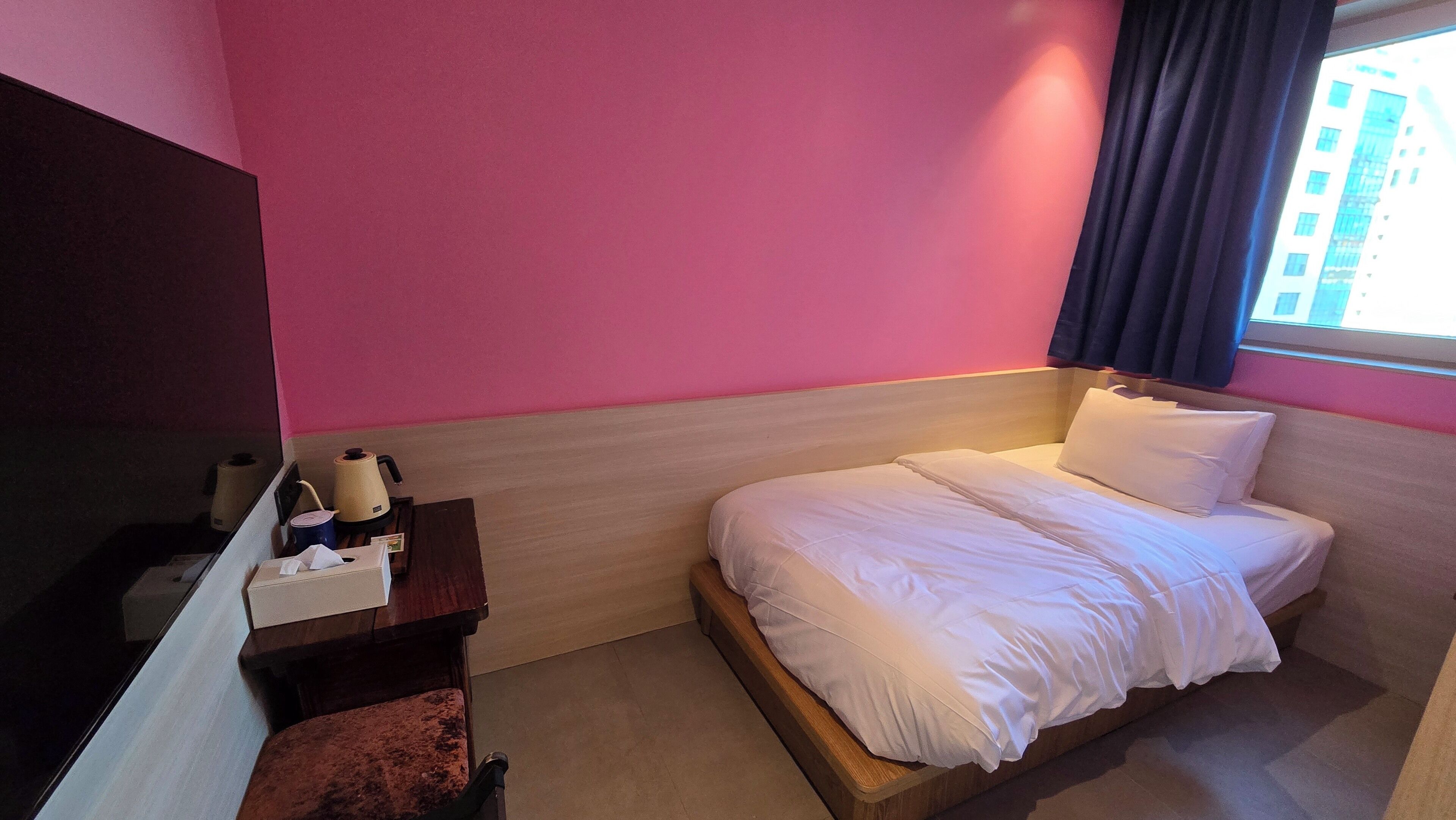 Una habitación de hotel con cama, un escritorio con silla y una ventana con cortinas.
