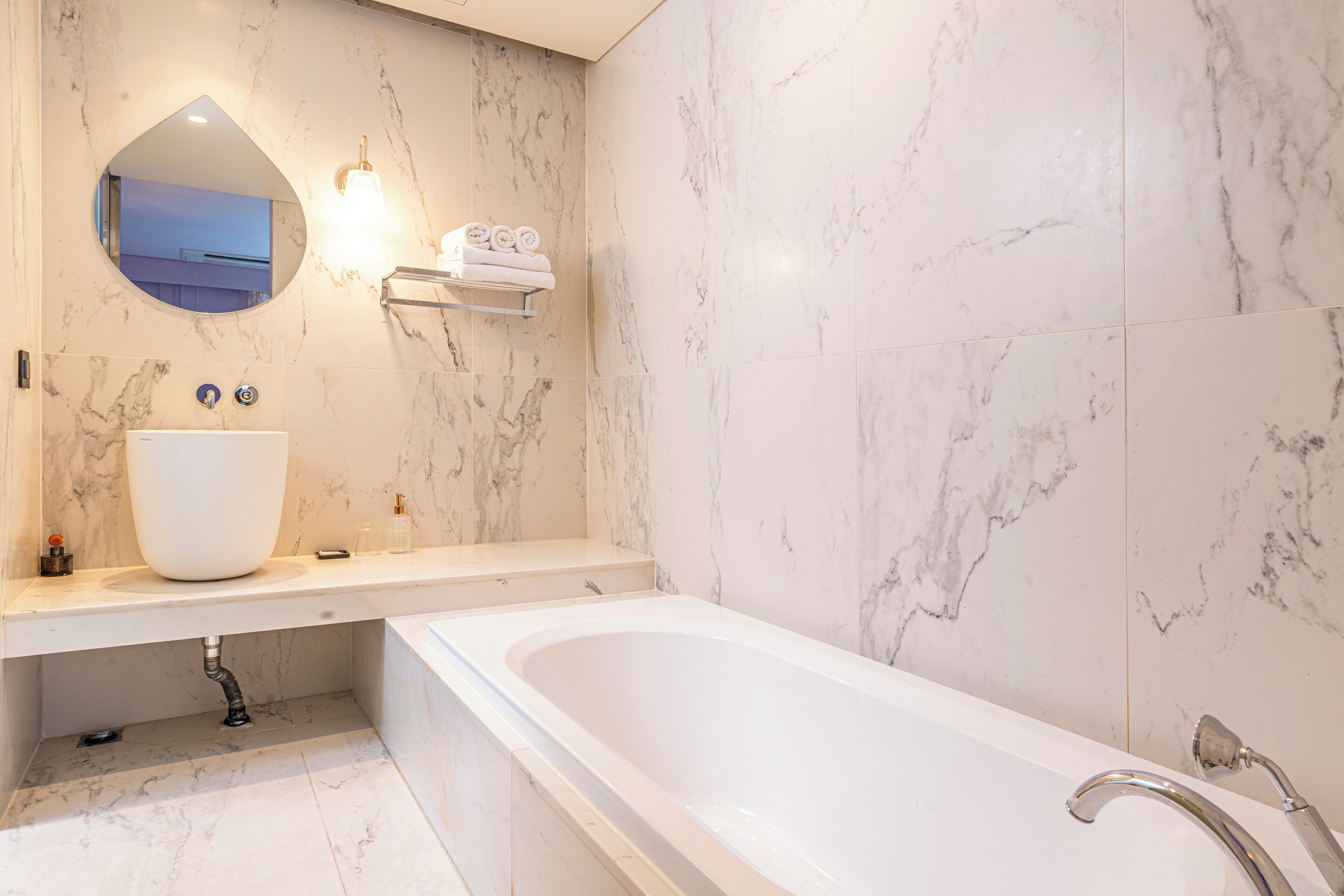 A modern bathroom with a large bathtub, a round mirror, and a marble wall.