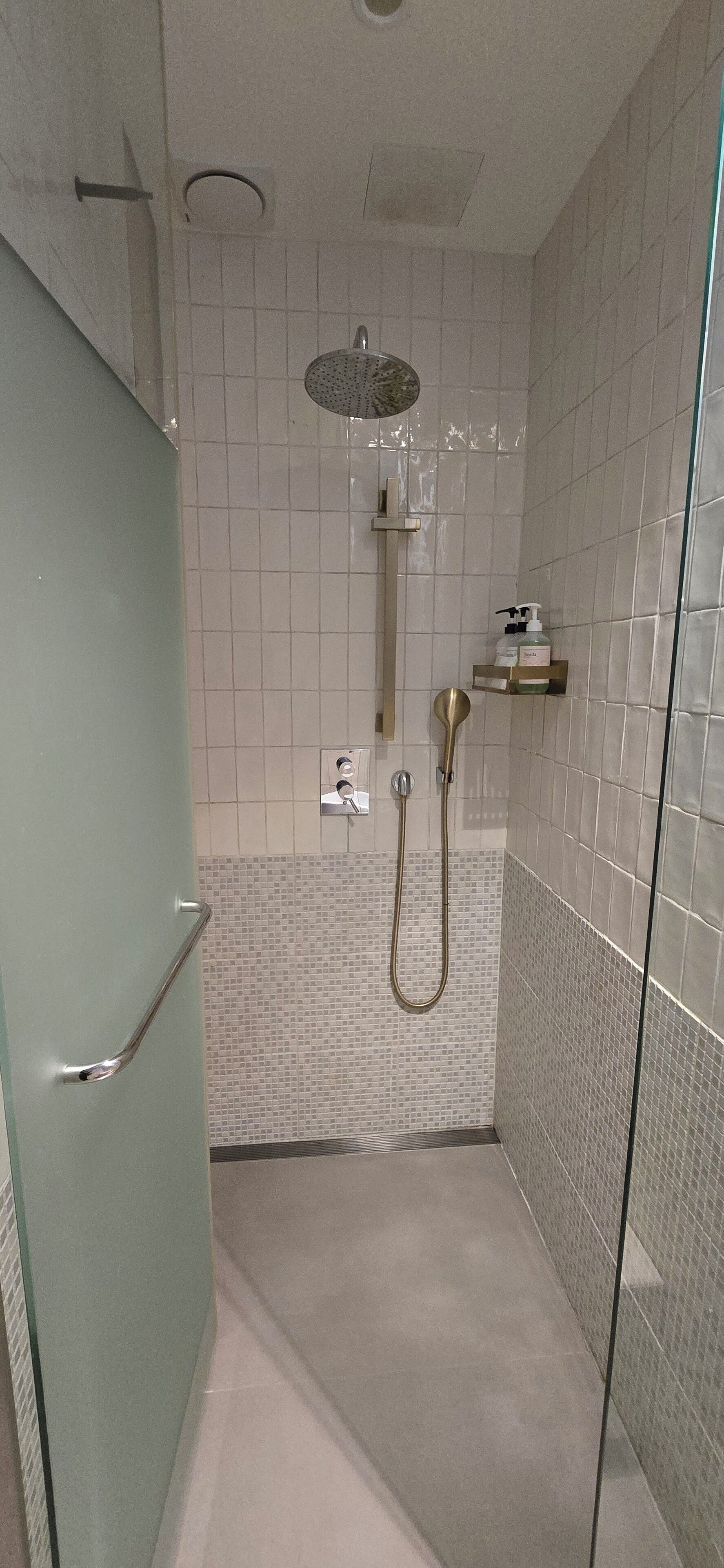 A modern bathroom with a glass shower enclosure, a handheld showerhead, and a wall-mounted faucet.