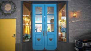 Puertas dobles azules con paneles de vidrio, una puerta amarilla a la izquierda y un coche negro estacionado a la derecha.