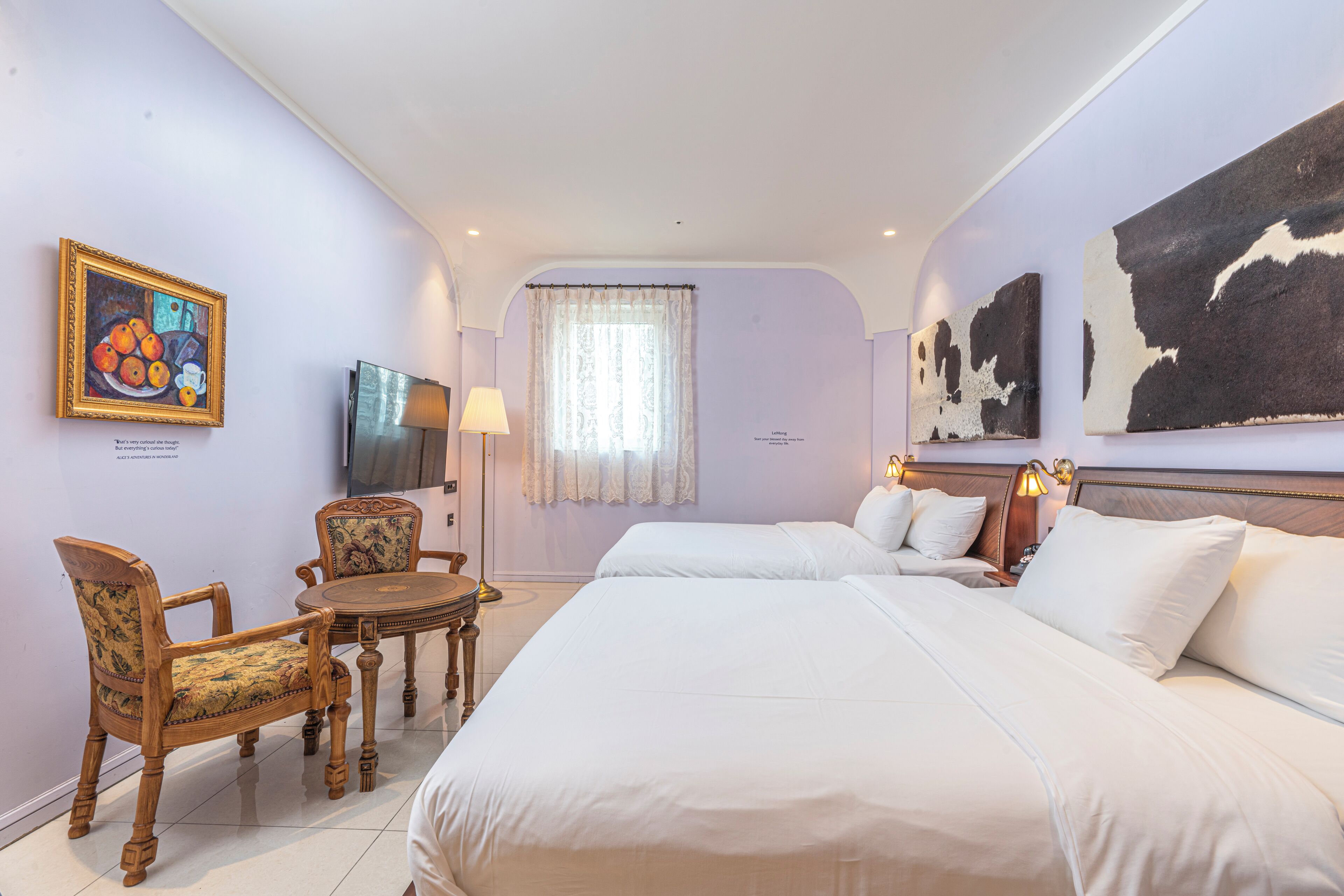A hotel room with two beds, a dining table with chairs, a TV, and artwork on the walls.