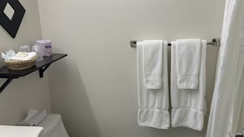Une salle de bain comprenant des toilettes, un lavabo, un porte-serviettes avec deux serviettes, un rideau de douche et une étagère avec des articles de toilette.