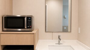 Un baño pequeño con microondas, lavamanos y espejo.