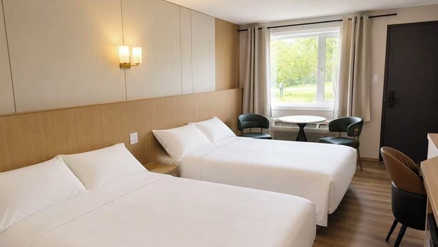 Habitación de hotel con dos camas, una mesita, sillas y una ventana con cortinas.