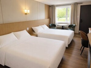 Habitación de hotel con dos camas, una mesita, sillas y una ventana con cortinas.