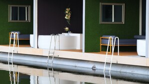 A modern spa area with a large bathtub, two seating areas, and a small window.