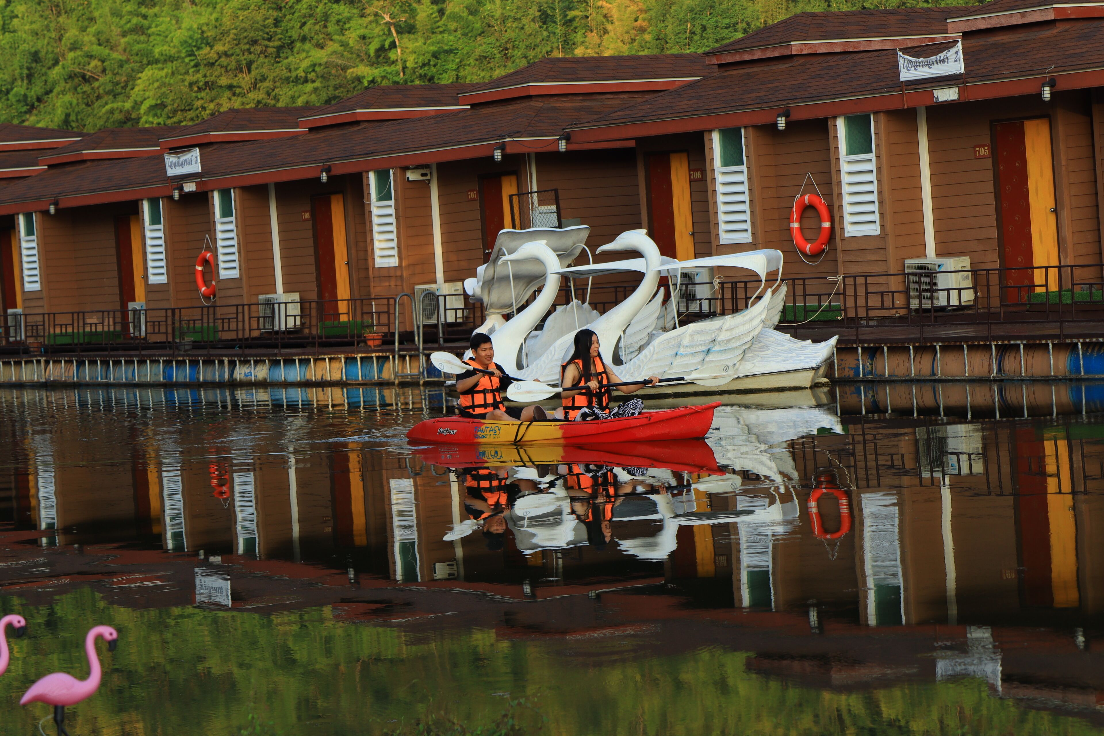 A row of cabins with a reflection in the water, a life preserver hanging on the wall, and a swan sculpture.