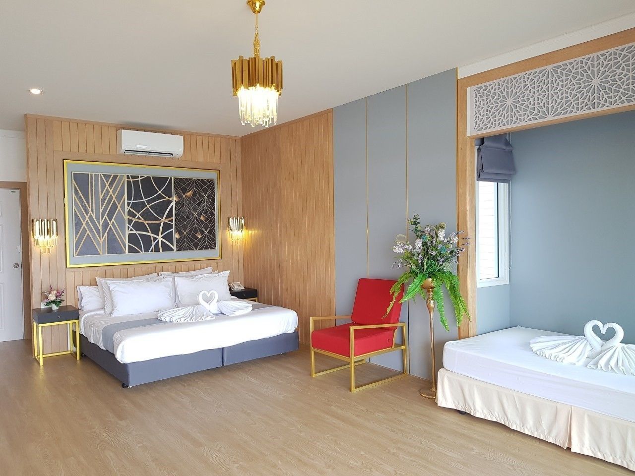 Ein modernes Hotelzimmer mit einem großen Bett, einem kleineren Bett, einem roten Sessel und einer Wandverkleidung.