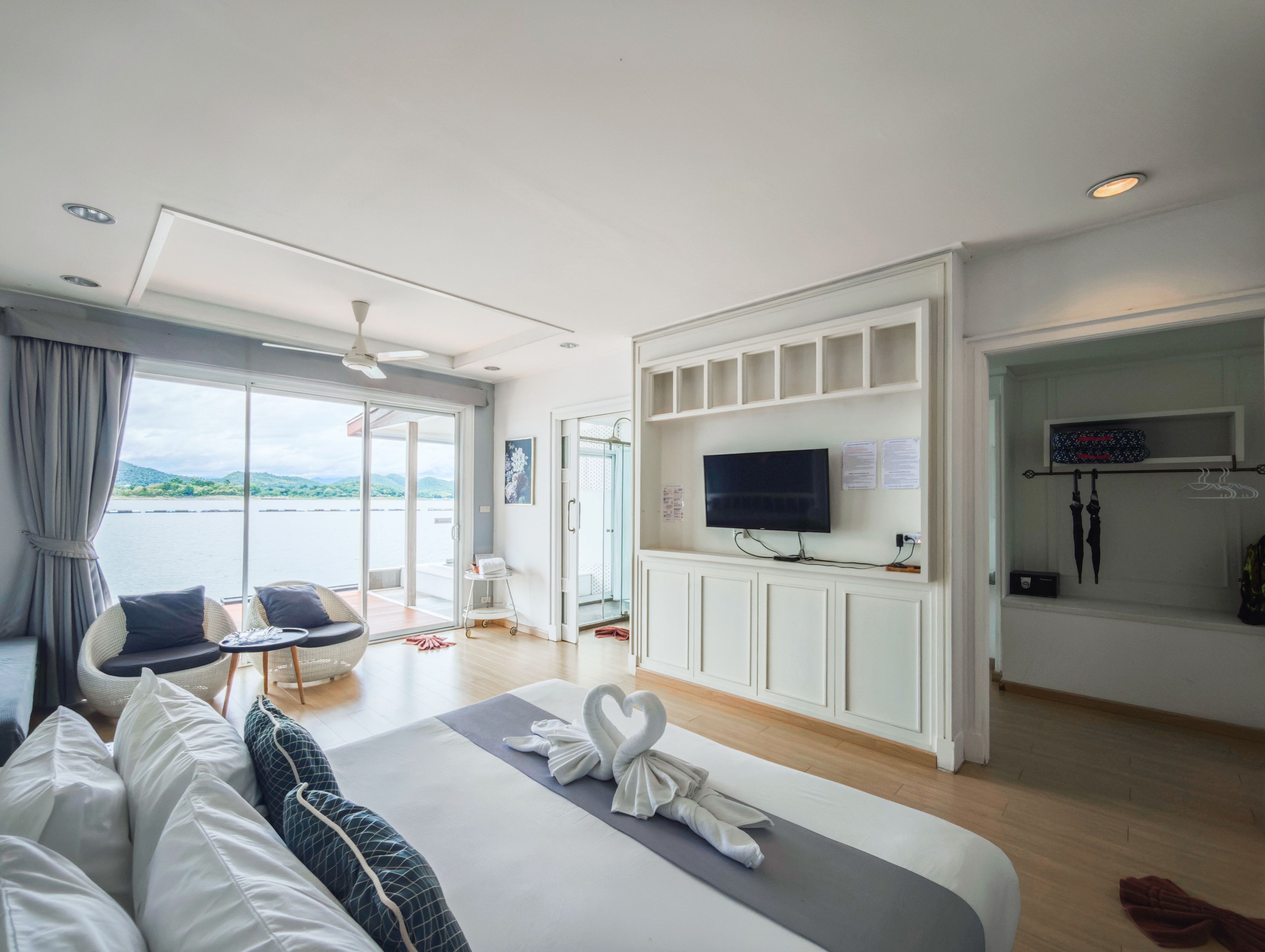 Una habitación de hotel moderna con cama, televisor, zona de estar con sillas, vistas al exterior y zona de ducha.