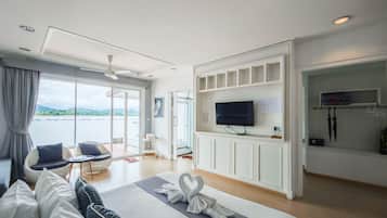 Una habitación de hotel moderna con cama, televisor, zona de estar con sillas, vistas al exterior y zona de ducha.