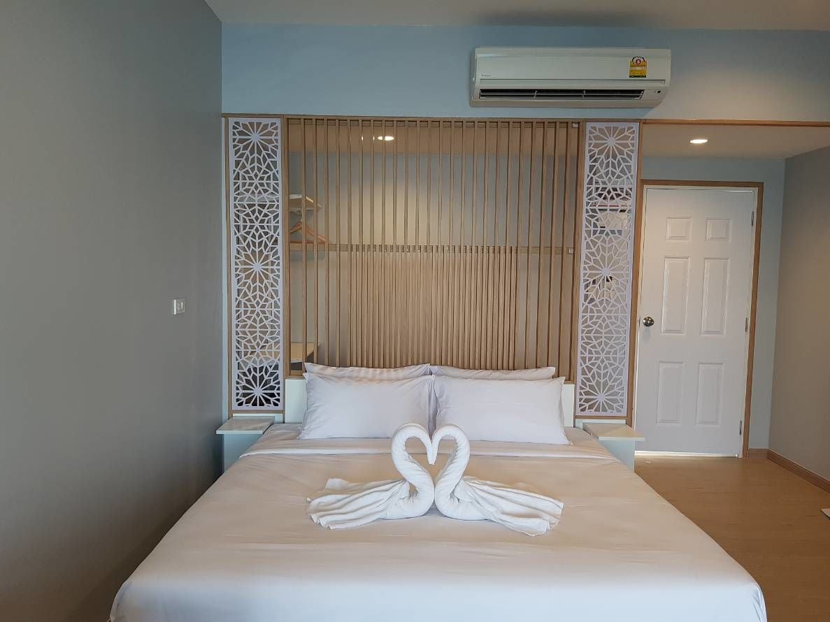 Une chambre d’hôtel avec un lit, du linge de lit blanc, une serviette pliée en forme de cœur, un appareil de climatisation et des panneaux décoratifs.