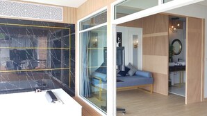 A modern room with a large glass door leading to a bathroom, a blue sofa, and a wooden floor.