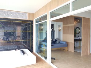 A modern room with a large glass door leading to a bathroom, a blue sofa, and a wooden floor. - Raya Buri Resort (Si Sawat)