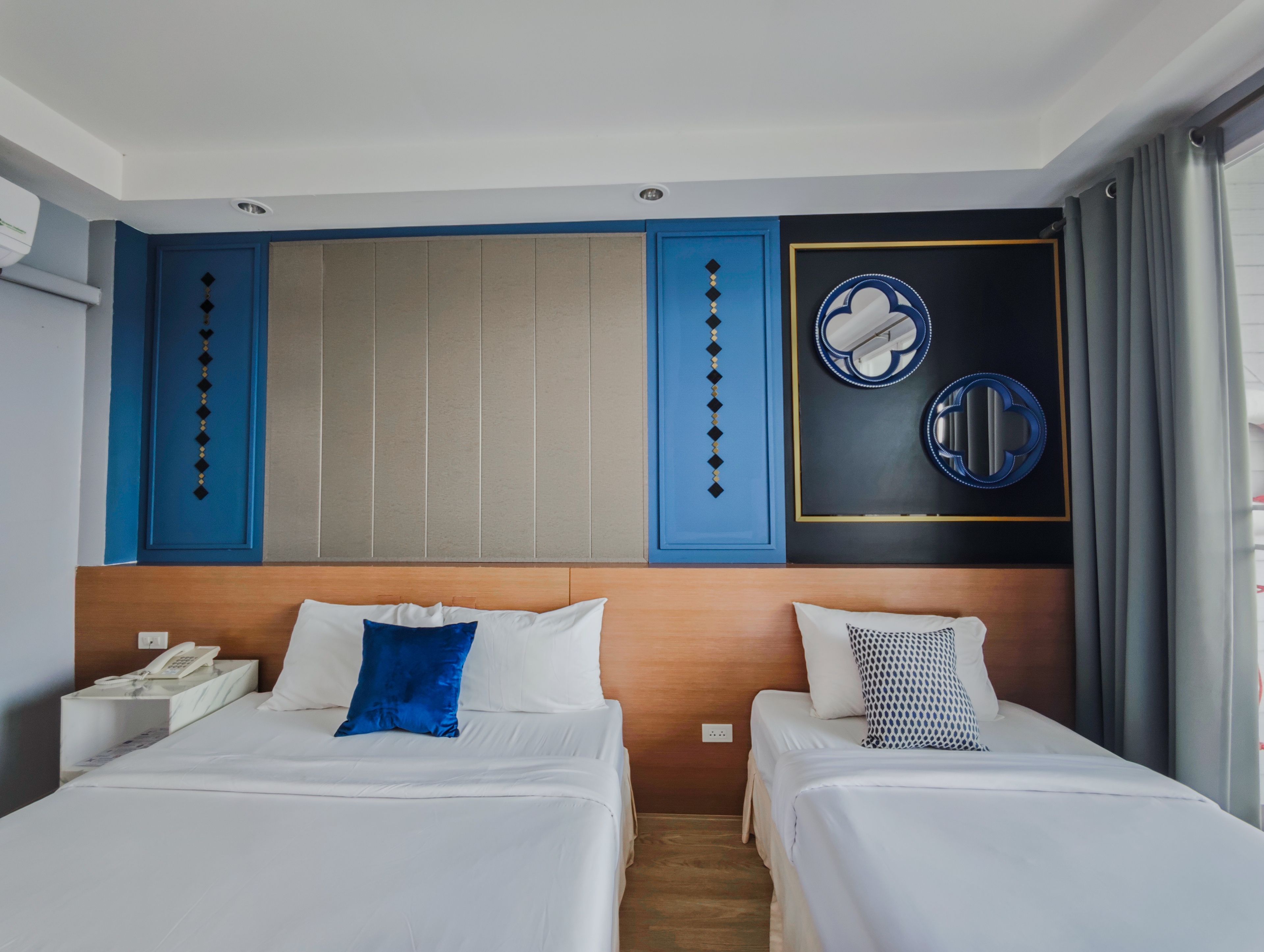 Une chambre d’hôtel avec deux lits, une tête de lit en bois, un téléphone fixé au mur et un miroir décoratif.