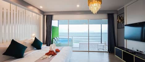A modern hotel room with a large bed, a chandelier, a TV, and a balcony with a view of the sea.