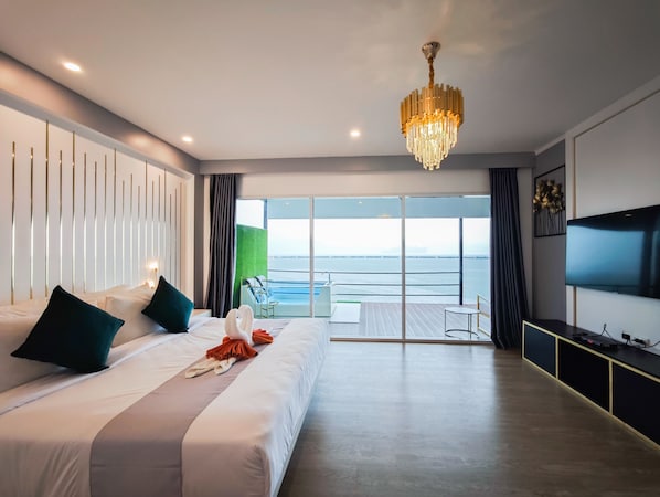 A modern hotel room with a large bed, a chandelier, a TV, and a balcony with a view of the sea.