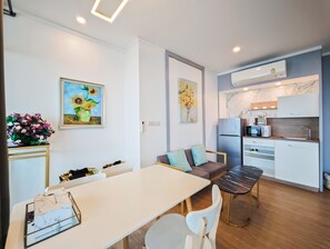 Eine moderne Küche mit Kühlschrank, Mikrowelle und Kaffeemaschine. Ein Esstisch mit Stühlen und eine Couch mit Kissen sind ebenfalls vorhanden.