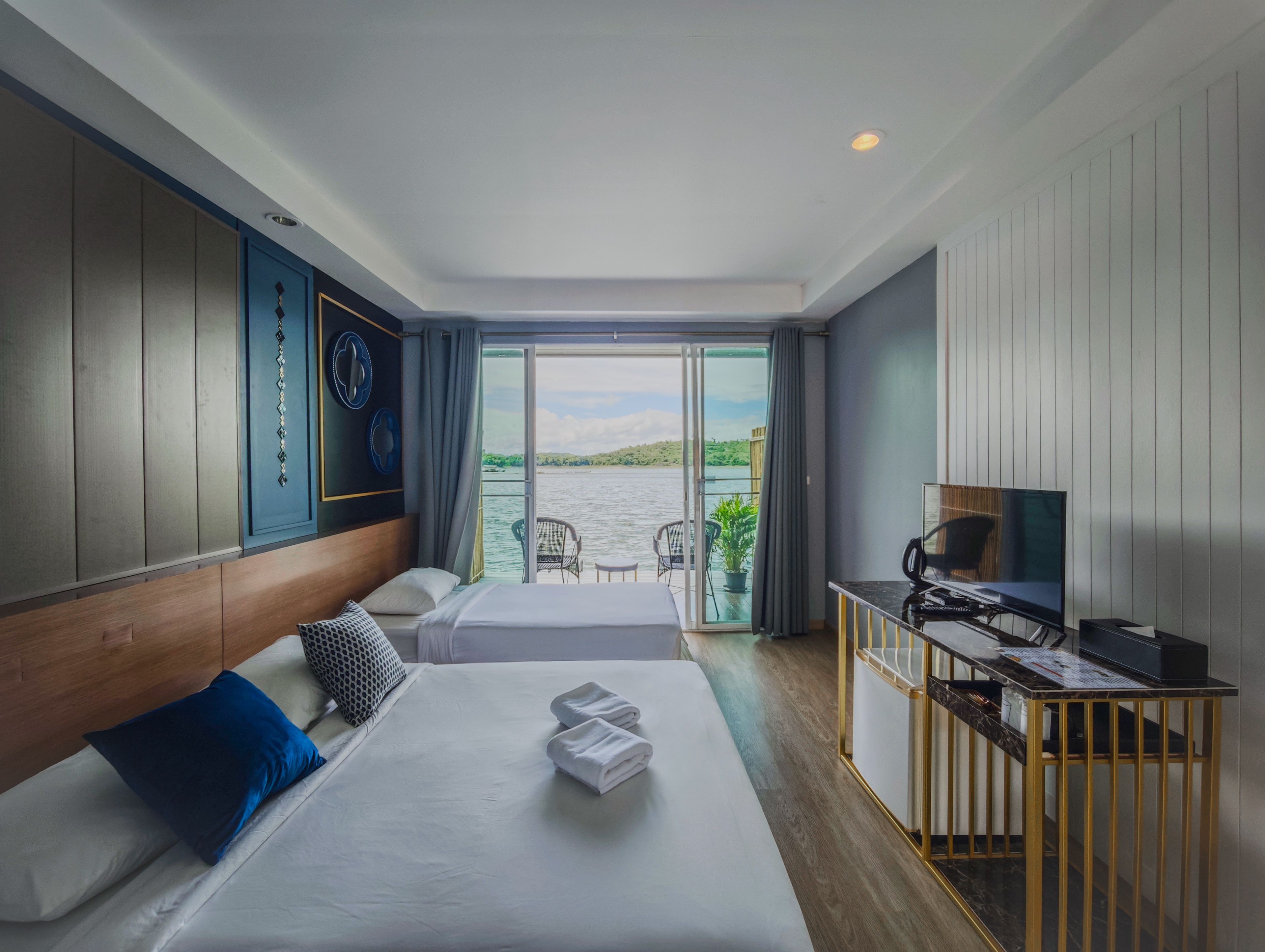 A hotel room with a bed, a desk with a television, and a view of a body of water through a sliding door.