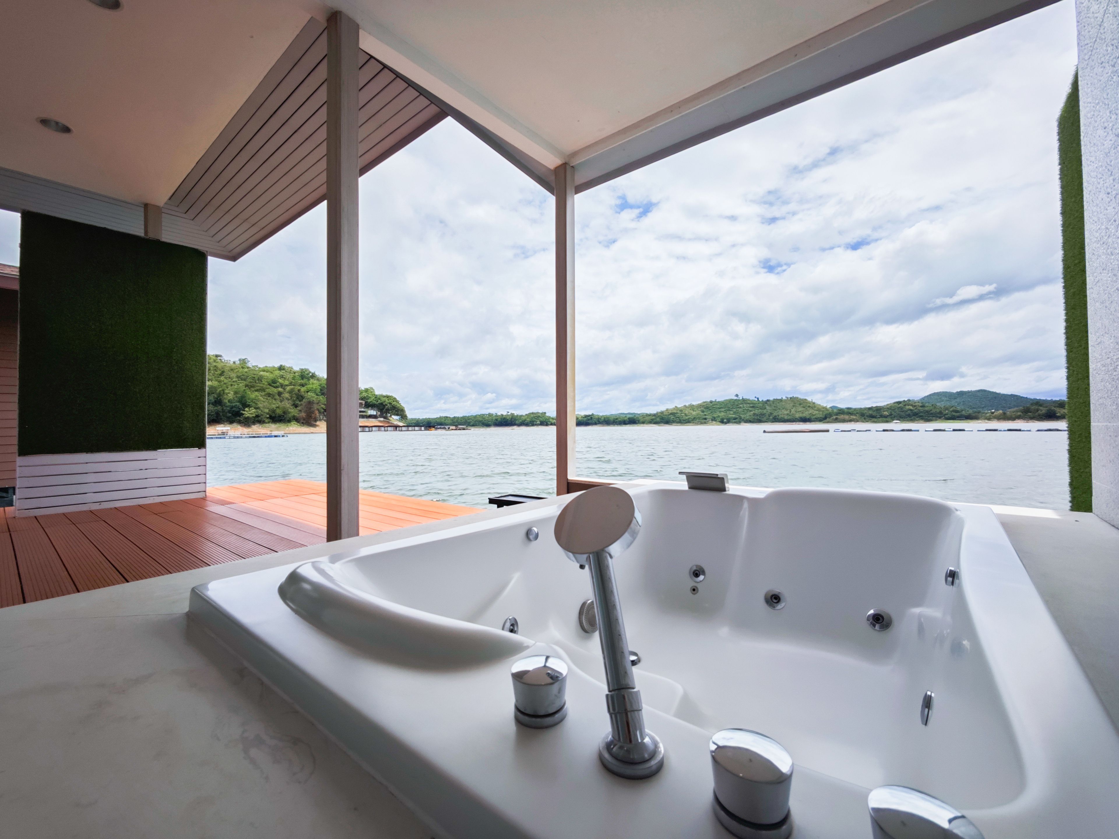 Une salle de bain moderne avec une grande baignoire, une terrasse en bois et une vue sur un lac, avec des collines à l'horizon.