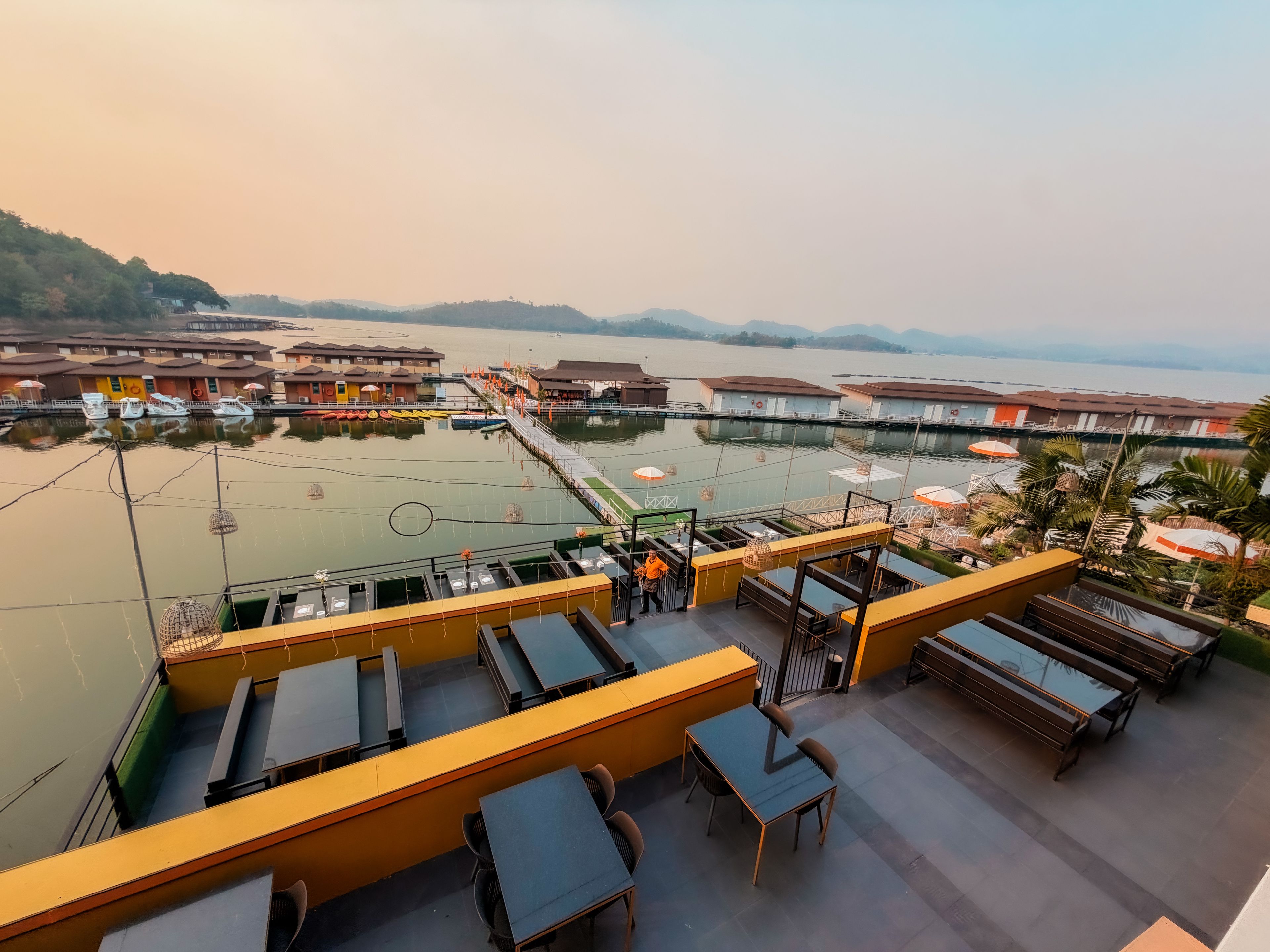 A terrace with tables and chairs overlooking a body of water with boats and a dock.