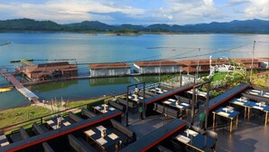 Restaurante à beira-mar com mesas ao ar livre, com vista para um lago, rodeado por colinas.