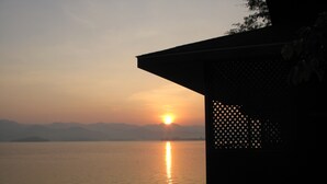 A serene sunset over a calm lake, viewed from a covered outdoor area with a lattice structure.