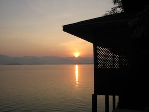 A serene sunset over a calm lake, viewed from a covered outdoor area with a lattice structure. - Raya Buri Resort (Si Sawat)