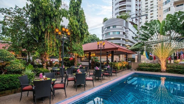 A poolside area with a covered seating area, outdoor dining, and a view of a modern building in the background.