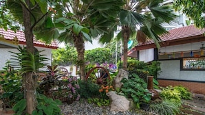 A garden with a variety of plants, a decorative wheel, and a rustic stone structure.