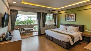A hotel room with a bed, a desk, a chair, a TV, and a balcony with curtains.