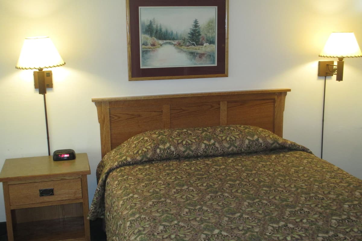 A neatly made bed with a patterned bedspread, a wooden headboard, and two bedside lamps on either side.
