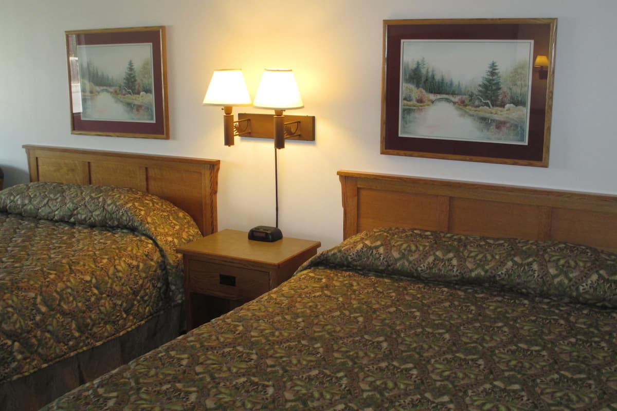 A hotel room with two beds, a nightstand, a lamp, and two framed pictures on the wall.
