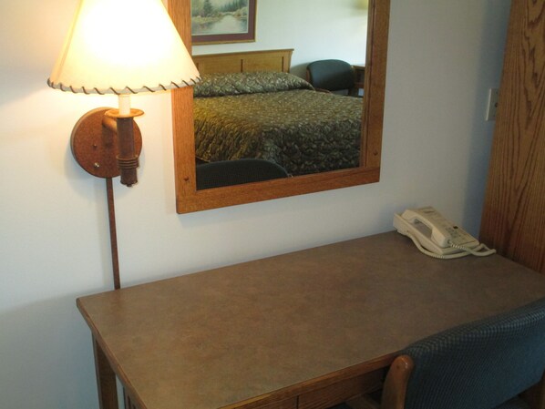 A hotel room with a wooden desk, a lamp, a mirror, a telephone, and a bed with a patterned bedspread. - Bozeman Inn (Bozeman)