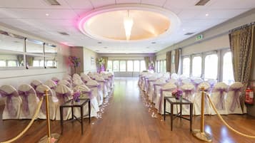 A spacious hall with a wooden floor, rows of chairs with purple sashes, a central aisle, and a chandelier.