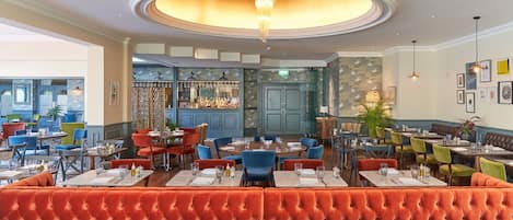 A restaurant with a central bar area, multiple seating options including booths and tables, and a chandelier.