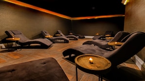A spa room with multiple reclining chairs, wooden side tables, and candles.