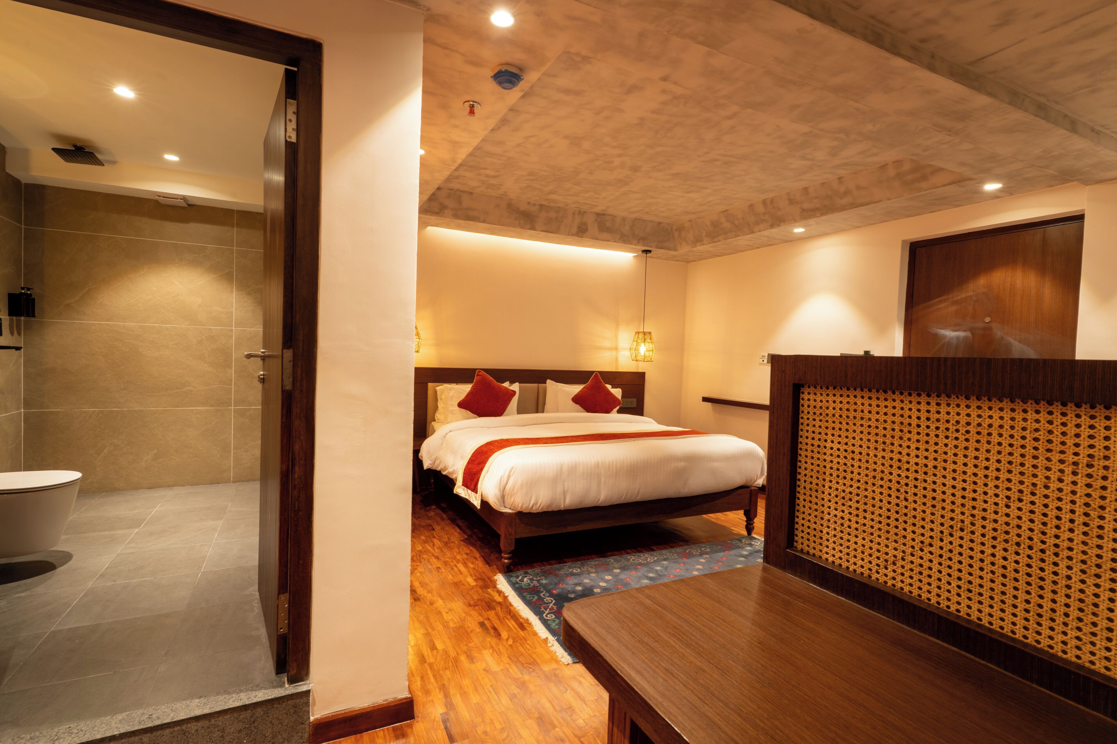 A hotel room with a wooden bed, a wooden nightstand, a bathroom with a shower, and a view of the cityscape.