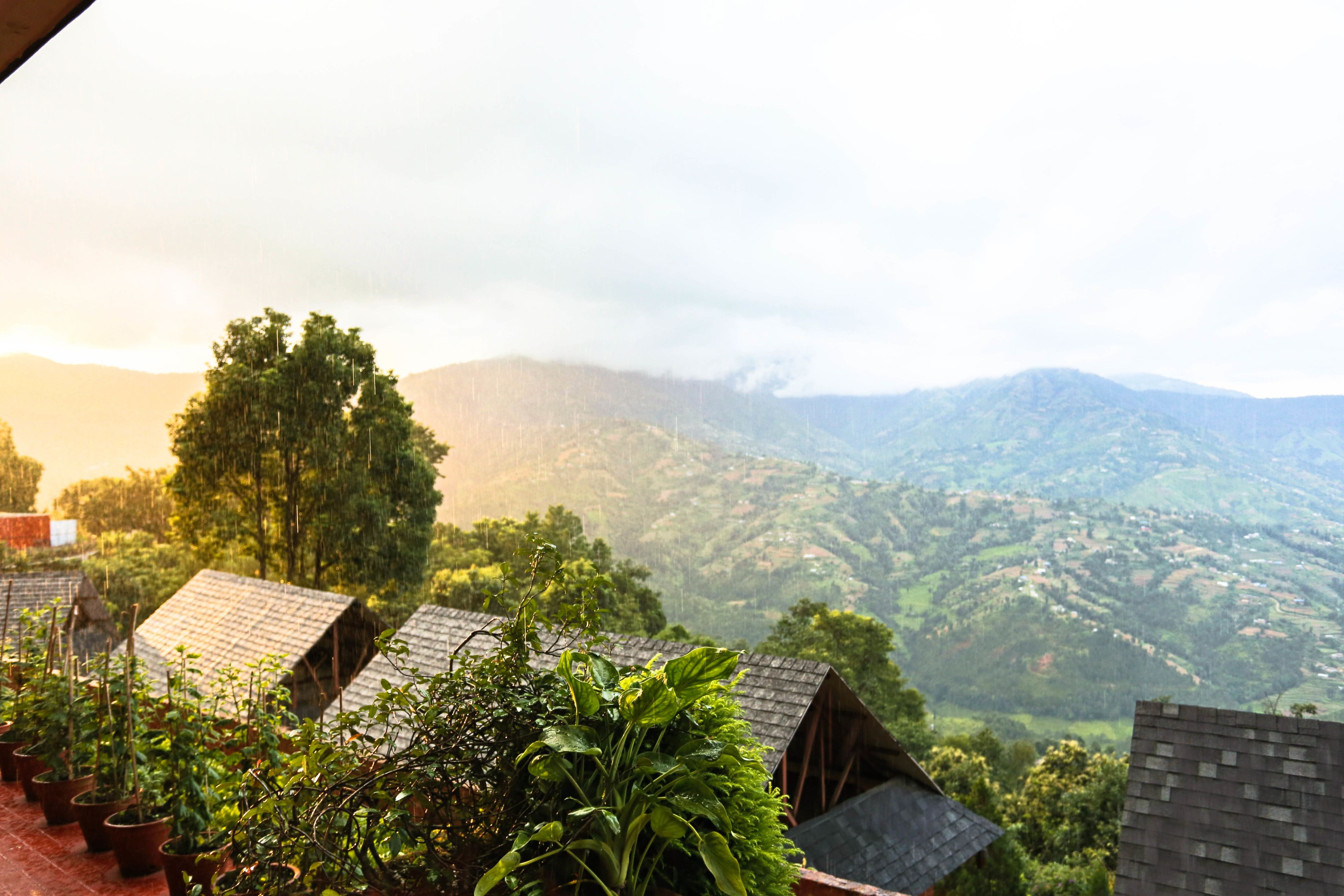 A view of a mountainous landscape with several houses with sloped roofs, surrounded by lush greenery and trees.