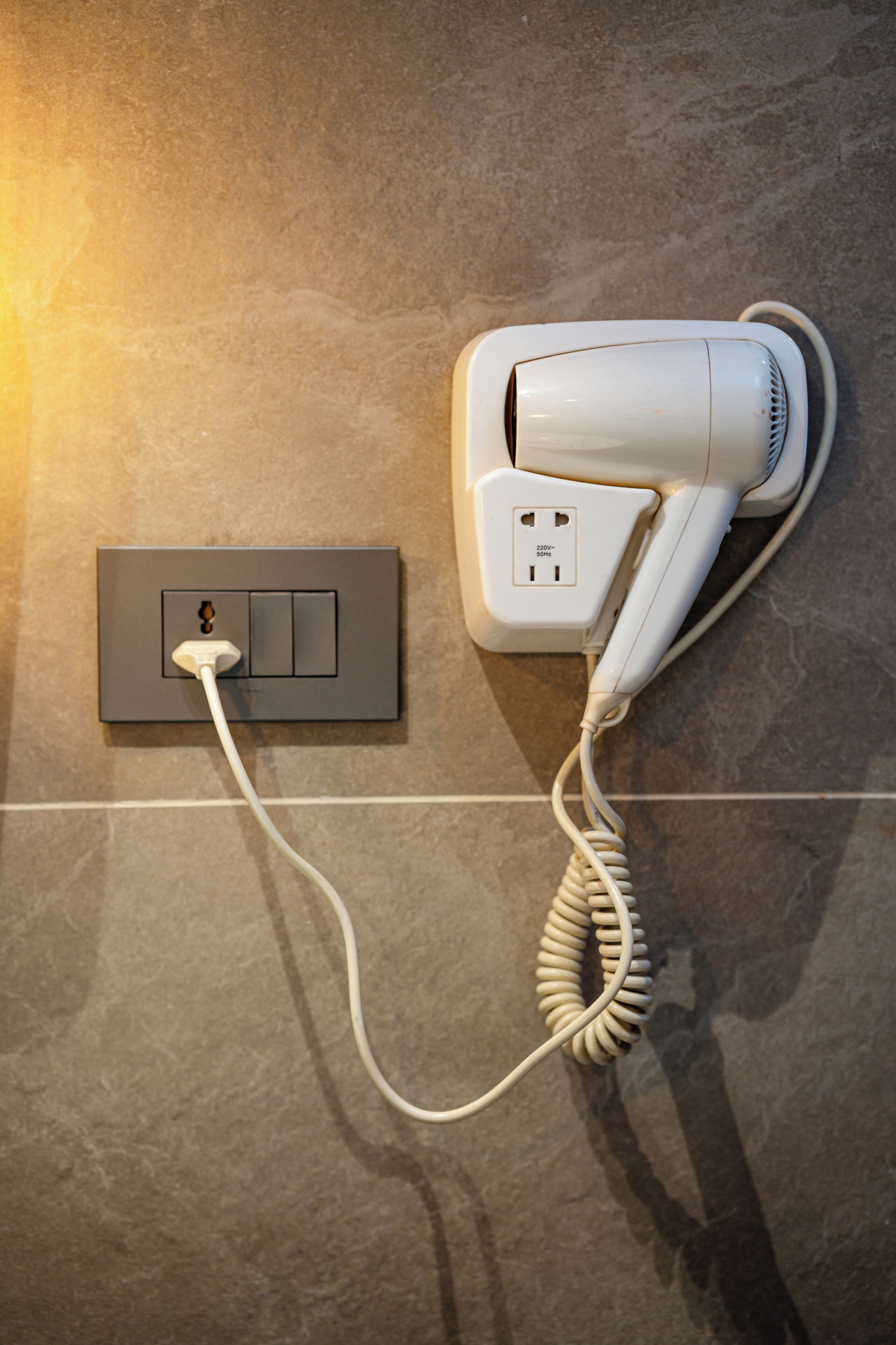 A hair dryer plugged into a wall socket on a tiled surface.