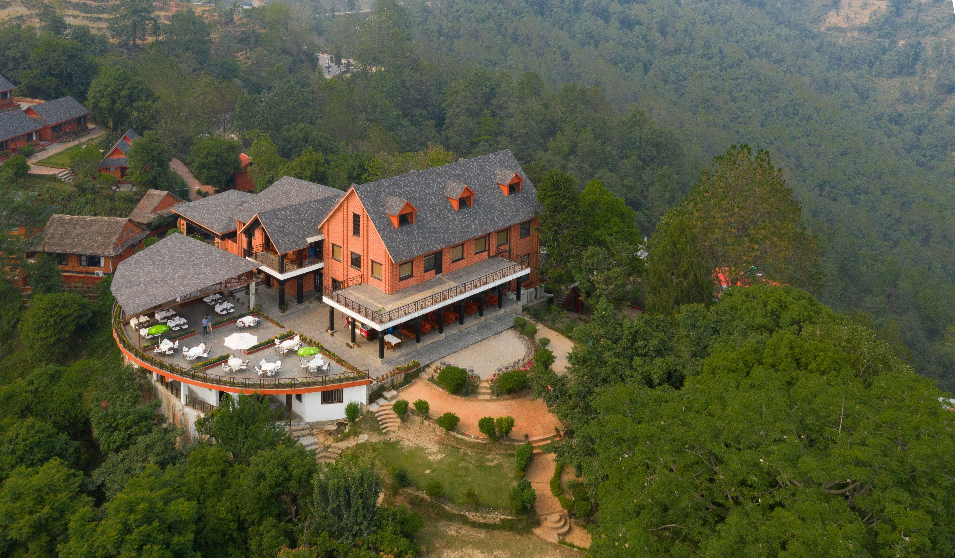 Un grand bâtiment à plusieurs étages, doté d’une cour intérieure et d’un espace extérieur aménagé pour s’asseoir, le tout entouré d’une forêt dense.