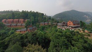 A hillside resort with multiple red-roofed buildings, surrounded by dense forest and mountains.