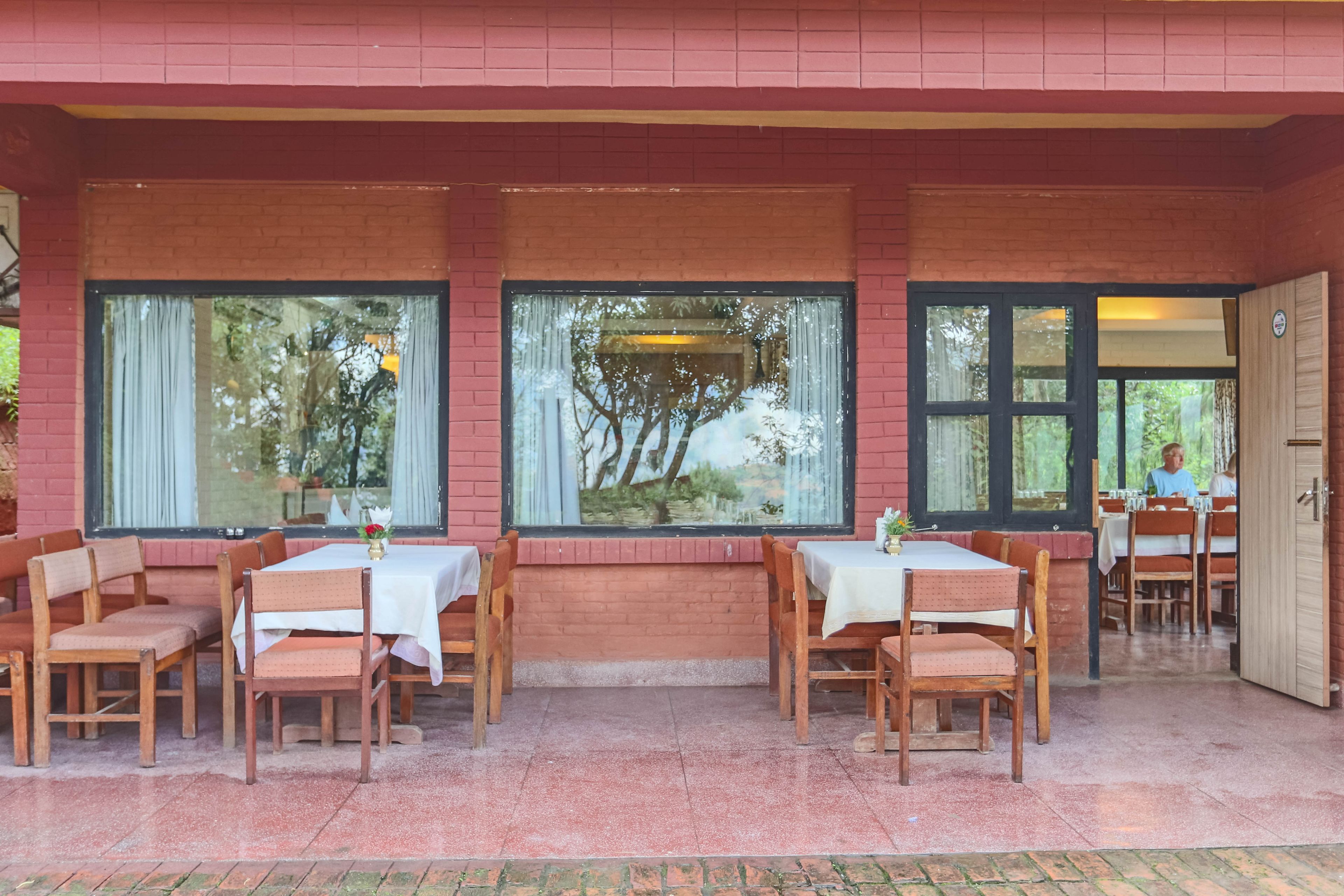 Un área de comedor al aire libre con paredes de ladrillo, ventanas amplias y mesas y sillas de madera.